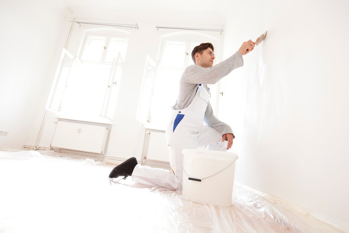 Maler streicht eine Wand in einem Zimmer weiß